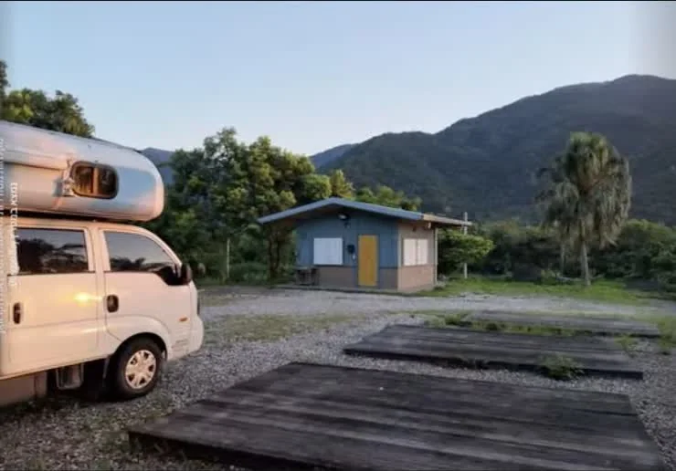 白色露營車停在花蓮山腳營位，旁邊有木平台、椰子樹與綠色山景