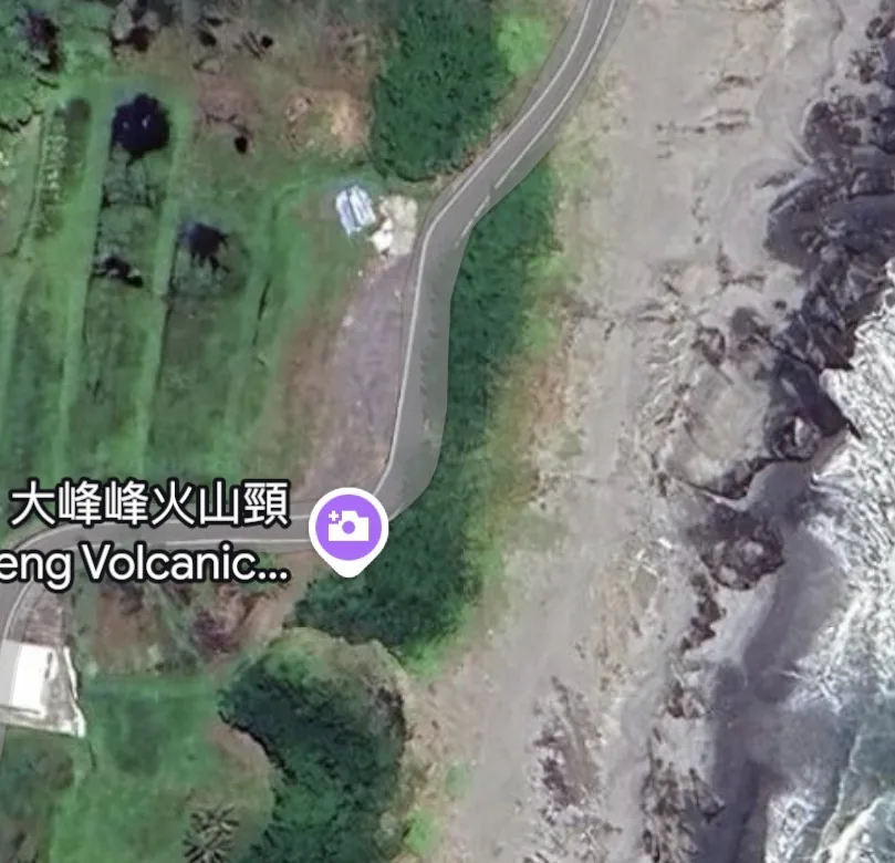 Close satellite view of a coastal side road, an open roadside area and a rocky shore