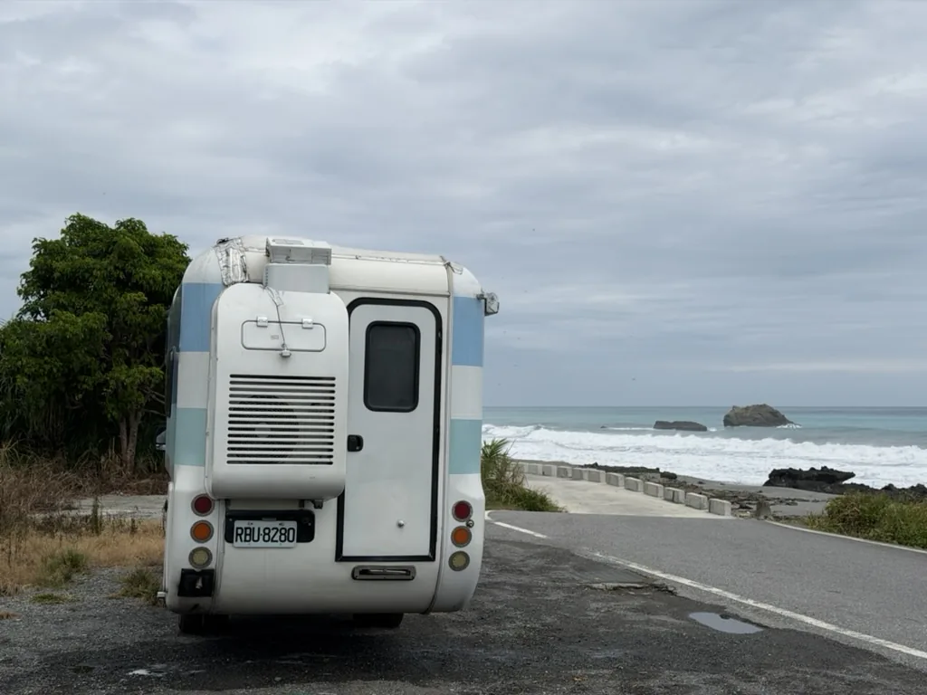 Rear view of the campervan facing a coastal side road and the Pacific Ocean, fully outside the traffic lane